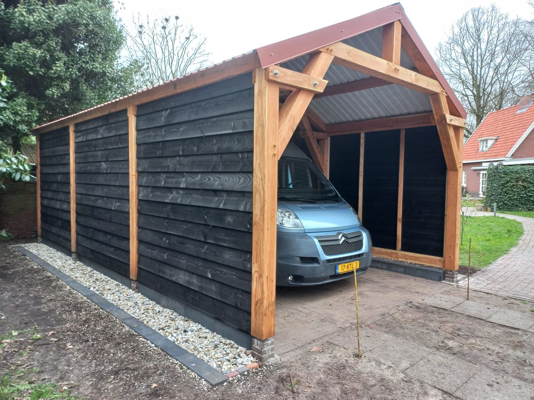 Langgerekte carport met zwarte zijwand en een bestelbus op de oprit