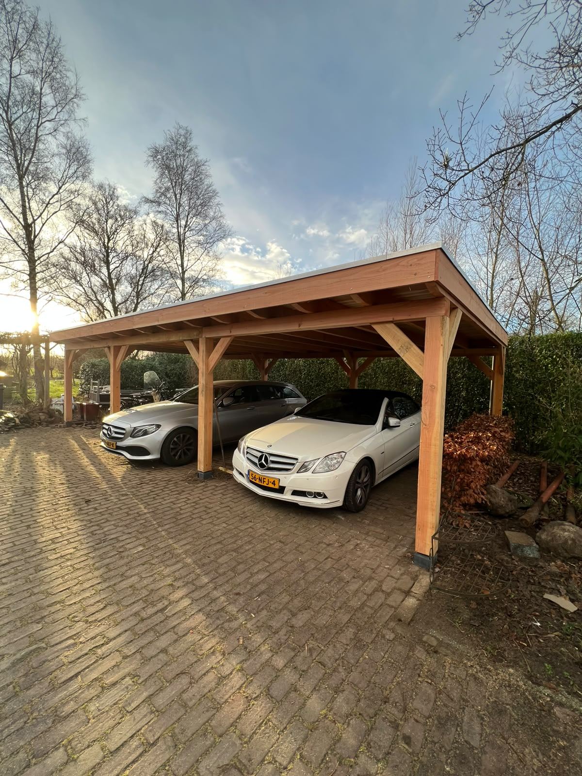 Twee auto's onder een douglas carport met plat dak in het late middaglicht