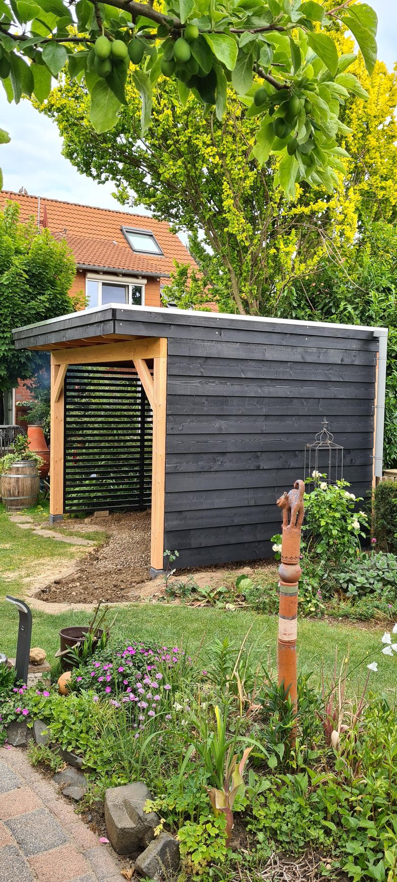 Zwart geschilderd tuinhuis met douglas hoekstijlen in een bloeiende tuin